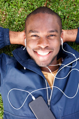 Wall Mural - above of smiling young black man lying on grass listening to music with earphones