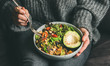 Leinwandbild Motiv Healthy vegetarian dinner. Woman in jeans and warm sweater holding bowl with fresh salad, avocado, grains, beans, roasted vegetables, close-up. Superfood, clean eating, vegan, dieting food concept