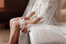 Woman Wearing A Garter On The Leg. The Bride Holds In Hand Lose-up Garter In Hotel Room. Morning Preparation Wedding Concept.