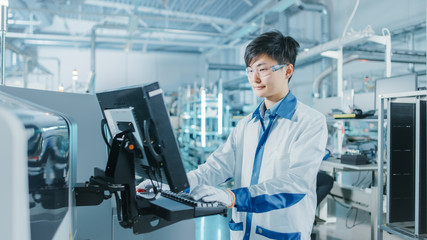 On High Tech Factory Asian Engineer Uses Computer for Programing Pick and Place Electronic Machinery for Printed Circuit Board Surface Mount Assembly Line. Production of PCB with SMT Machinery.