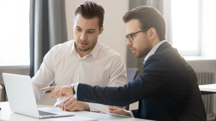 Wall Mural - Serious businessman pointing at laptop discussing corporate software with colleague