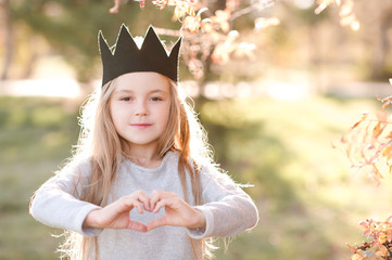 Wall Mural - Smiling baby girl 4-5 year old showing heart with fingers outdoors. Looking at camera. Spring season.