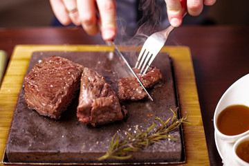 sirloin steak on a very hot stone being cooked by a man to his own taste on a wooden table with a kn