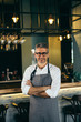© cherryandbees - senior barman crosses arms standing in front of counter in cafeteria