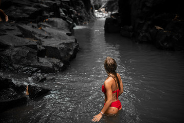 fashion portrait of beautiful woman with brunette hair in red swimwear posing  in river of waterfall in Bali