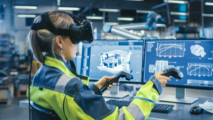 Wall Mural - Factory: Female Industrial Engineer Wearing Virtual Reality Headset and Holding Controllers, She Uses VR technology for Industrial Design, Development and Prototyping in CAD Software.