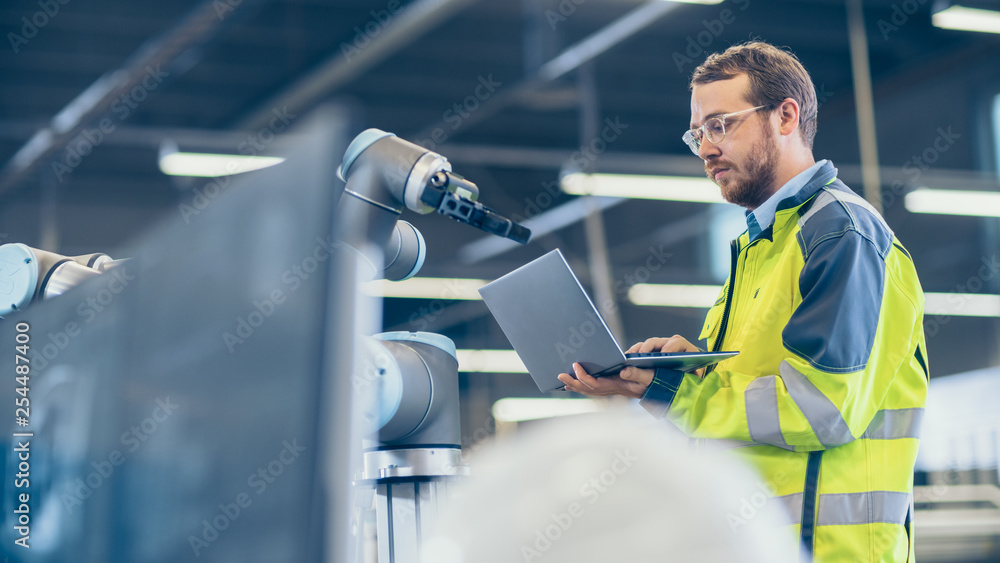 At the Factory: Automation Engineer Uses Laptop for Programming Robotic ...
