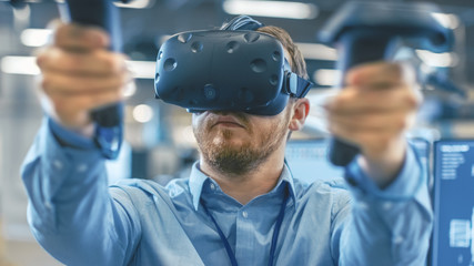 Fototapete - Portrait Shot of the Industrial Engineer Wearing Virtual Reality Headset and Using Controllers, ready to Work. In the Background Manufacturing Plant and Monitors.