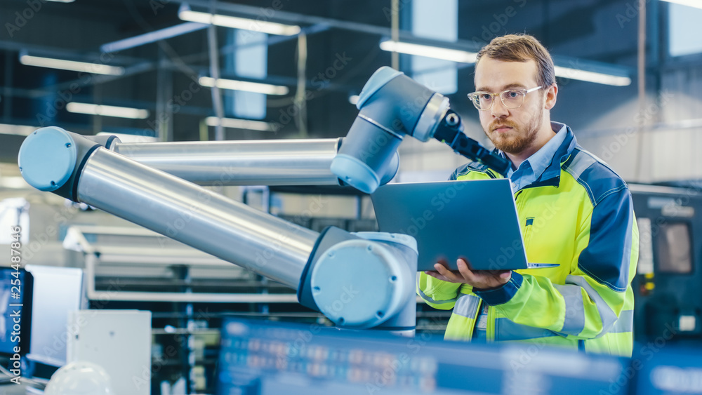 At the Factory: Automation Engineer Uses Laptop for Programming Robotic ...