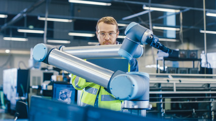 Poster - At the Factory: Automation Engineer Uses Laptop for Programming Robotic Arm. New Era in Automatic Manufacturing Industry.