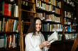 © proimagecontent - Young attractive student girl reading a book between library bookshelves