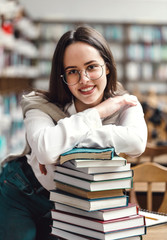 Wall Mural - Girl standing with hands folded on books in library