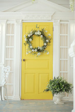 Beautifully Decorated Farmhouse Look. Bright Yellow Door, A Spring Greenery Wreath Of Flowers, A Pot With Green Plants. Rustic Interior Element Of Spring Porch