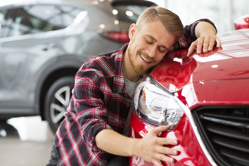 Happy handsome man buying a new car at the dealership