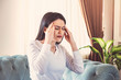 © erhanyelekci - Young woman suffering from strong headache or migraine sitting at home, millennial guy feeling intoxication and pain touching aching head, morning after hangover concept