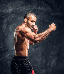 professional fighter showing kick fighting technique. studio photo against a dark textured wall