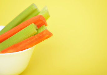 Wall Mural - Fresh green celery and carrots on yellow background