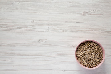 Hulled sunflower seeds in a pink bowl over white wooden background, top view. Flat lay, overhead, from above. Copy space.