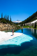 A Female Backpacker Stands On A Floating Shelf Of Snow Melt On A Small Lake Along The East Lostine River Trail (#1662) In The Eagle Cap Wilderness Of The Wallowa Mountains In Northeast Oregon. The Iconic Eagle Cap Peak Is In The Background.