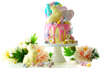 On-trend Easter theme candy land drip cake decorated with lollipops, candy eggs and white chocolate bunny in party table setting.