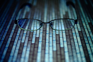 Wall Mural - reading data in digital age. glasses and flowing binary code matrix. shallow depth of field image of glasses on display panel. multiple lines of blue code moving under glasses.