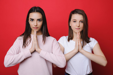 portrait of two adult cute female looking at camera and thanking with hands toeghether in front of a