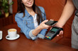 © New Africa - Woman using terminal for contactless payment with smartphone in cafe, closeup