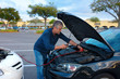 © Michael O'Keene - A man is jump starting a car with jumper cables helping person with a disabled automobile due to a dead battery at a shopping mall parking lot.