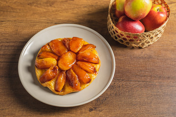 Wall Mural - Apple Tarte Tatin on a plate with red apple in basket as props.