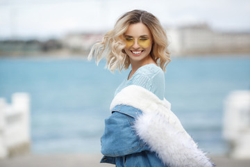 The girl enjoying the warm autumn day.Portrait of beautiful girl near the water.Portrait of a beautiful woman in a blue jacket outdoors in early spring on the ocean coast.Spring portrait on the beach.