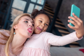 Girl and funny woman showing tongues making photo