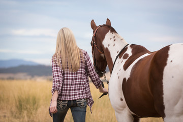 Young blonde girl walking with horse