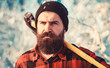 Bearded lumberjack. Male holds an ax on a shoulder. Brutal bearded man. Brutal bearded lumberjack with ax in winter forest. Lumberjack with an ax in his hands. Handsome man, hipster in snowy forest.