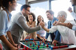 © NDABCREATIVITY - Business people having great time together.Colleagues playing table football in office.