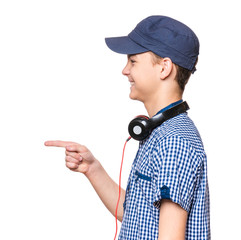 Poster - Portrait of young Student with Cap and Headphones, isolated on white background. Teen Boy smiling, looking away and points his Finger at something.