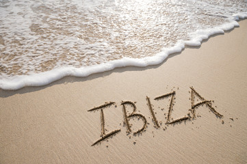 Wall Mural - Simple Ibiza Spanish holiday getaway message written in smooth sand with an incoming wave on a tropical beach