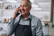 © Yakobchuk Olena - Joyful senior man in apron talking on cellphone