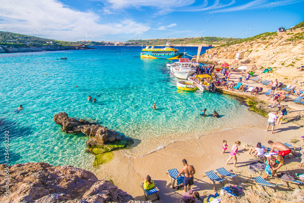 Comino, Malta - November, 2018: Tourists crowd at Blue Lagoon to enjoy the clear turquoise water on a sunny summer day with clear blue sky and boats on Comino island, Malta. - obrazy, fototapety, plakaty 