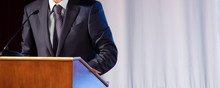 Speech Of An Abstract Man In A Suit On Stage At The Stand For Performances. Tribune Or Cathedra For Speaker Official, President Or Professor. Close-up. Copy Space.