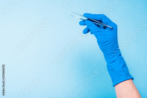 Fotografía Hand in blue glove holding dental tweezers on light blue background