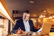 © Dusan Petkovic - Middle aged CEO dressed smart casual writing in agenda schedule and sitting in cafeteria. In front of him laptop.