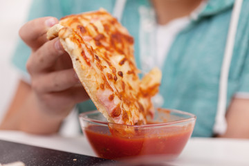 Hand dip a slice of pizza into tomato sauce in a bowl