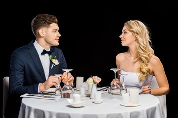 Wall Mural - handsome groom and beautiful bride sitting at served table isolated on black