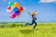 Glückliches Mädchen spring mit vielen bunten Luftballons über eine grüne Wiese