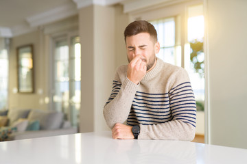 Canvas Print - Young handsome man at home smelling something stinky and disgusting, intolerable smell, holding breath with fingers on nose. Bad smells concept.