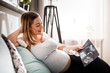 © leszekglasner - Pregnant woman on sofa looking her baby on ultrasound image, usg photo