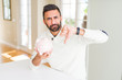© Krakenimages.com - Handsome hispanic man holding piggy bank with angry face, negative sign showing dislike with thumbs down, rejection concept