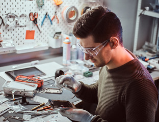 Wall Mural - The technician uses a magnifying glass to carefully inspect the internal parts of the smartphone in a modern repair shop