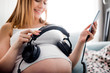 © leszekglasner - Beautiful cheerful pregnant woman holding headphones on belly showing music to baby