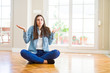 © Krakenimages.com - Beautiful young woman sitting on the floor at home clueless and confused expression with arms and hands raised. Doubt concept.